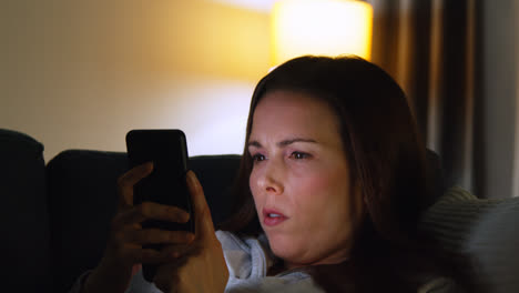 Close-Up-Of-Woman-Lying-On-Sofa-At-Home-At-Night-Streaming-Or-Looking-At-Online-Content-On-Mobile-Phone-1